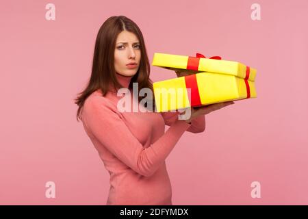 Launisch unglückliche Frau mit braunen Haaren in rosa Pullover enttäuscht von ihrem Geburtstagsgeschenk, hält ausgepackte Geschenkbox in den Händen. Studio-Sho Stockfoto