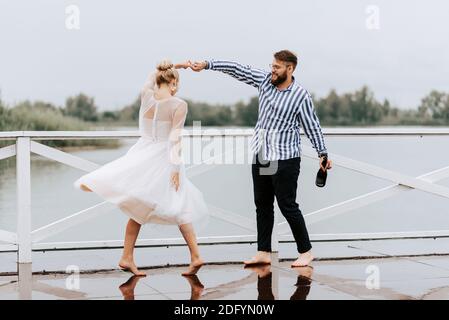 Ein Mann und eine Frau tanzen barfuß und haben Spaß auf dem Kai am See. Stockfoto