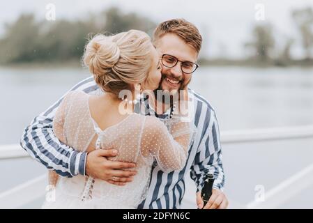 Die Braut und der Bräutigam küssen und umarmen auf dem Kai am Fluss. Stockfoto