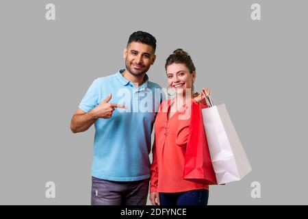 Zufriedene Käufer. Portrait von Happy bärtiger junger Mann in Freizeitkleidung auf Einkaufstüten, der in die Hände der aufgeregten Frau, mit Ermäßigungen. iso Stockfoto