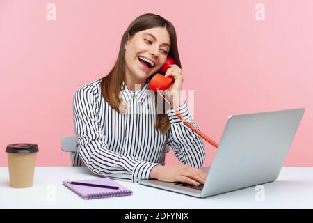 Lächelnd positive Frau Verkauf Manager erhält Anrufe auf Festnetz-Telefon und Bestellungen auf Laptop, Kommunikation mit Kunden am Arbeitsplatz sitzen. Stockfoto