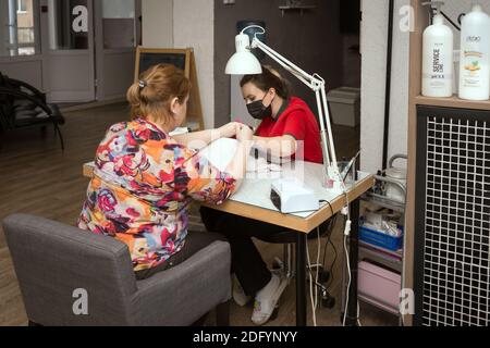 Ein professioneller Nageltechniker macht eine Maniküre für einen Klienten an einem Arbeitstisch in einem Haar- und Nagelsalon. Stockfoto