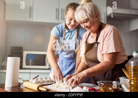 Zufriedene Großmutter, die ihre Enkelin ihr in der Küche helfen ließ Stockfoto