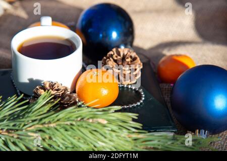 Kaffee in einer weißen Tasse mit Mandarinen mit Weihnachtsschmuck und Christbaumzweigen und Kegeln. Weihnachts-Set mit Kaffee Stockfoto