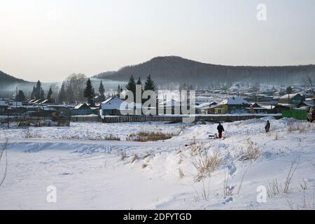 Eine rustikale Winterlandschaft mit Wanderkindern und einem gefrorenen Fluss im Vordergrund. Stockfoto