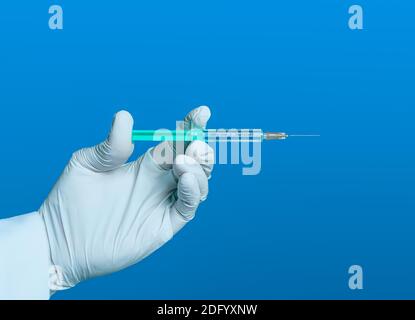 Hand mit Handschuh hält eine Spritze mit der deutschen Aufschrift Covid 19-Impfstoff vor blauem Hintergrund Stockfoto
