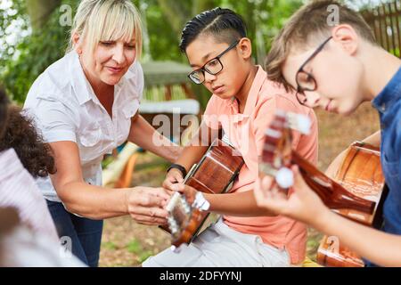 Lehrer hilft Kindern im Gitarrenunterricht im Sommerlager vor Talentshow Stockfoto