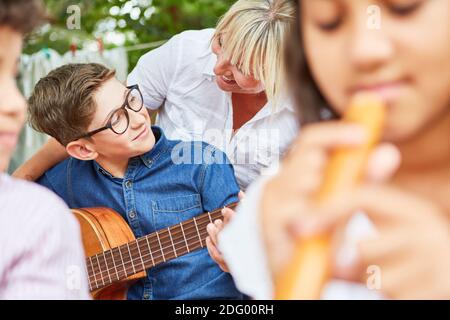 Lehrer hilft Kind mit Gitarre während Musikunterricht im Sommer Camp oder Sommercamp Stockfoto