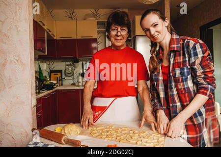 Junge Frau und ältere Mutter kochen Kekse in roten Kleidern. Stockfoto