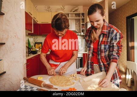 Junge Frau und ältere Mutter kochen Kekse in roten Kleidern. Stockfoto