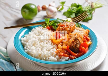 Moqueca baiana - brasilianische Fischeintopf mit Paprika, Limette, gehackte Tomaten, Kokosmilch, serviert auf einem Teller mit Langkornreis, Koriander auf einem ma Stockfoto