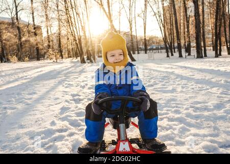 Kleiner Junge auf einem Schneemobil im Park. Sonnenlicht und Bäume mit Schatten auf dem Hintergrund. Stockfoto