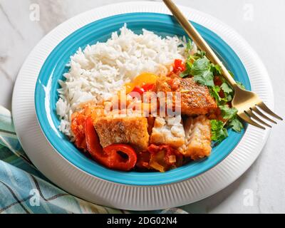 Moqueca baiana - brasilianische Fischeintopf mit Paprika, Limette, gehackte Tomaten, Kokosmilch, serviert auf einem Teller mit Langkornreis, Koriander auf einem ma Stockfoto