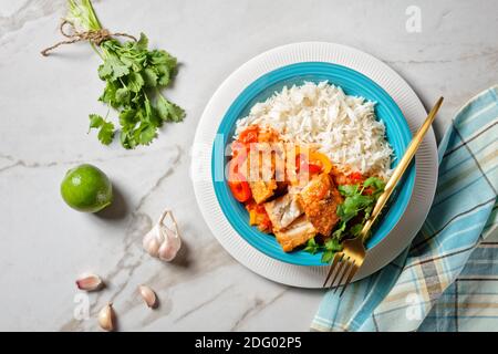 Moqueca baiana - brasilianische Fischeintopf mit Paprika, Limette, gehackte Tomaten, Kokosmilch, serviert auf einem Teller mit Langkornreis, Koriander auf einem ma Stockfoto