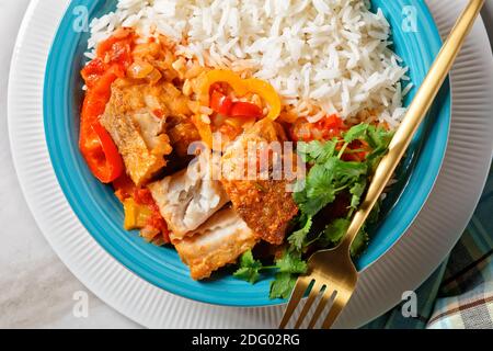 Moqueca baiana - brasilianische Fischeintopf mit Paprika, Limette, gehackte Tomaten, Kokosmilch, serviert auf einem Teller mit Langkornreis, Koriander auf einem ma Stockfoto