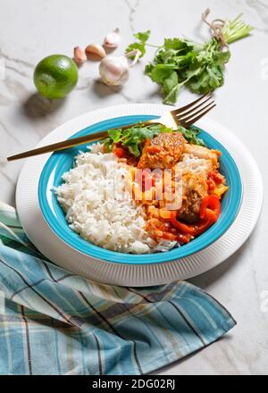 Moqueca baiana - brasilianische Fischeintopf mit Paprika, Limette, gehackte Tomaten, Kokosmilch, serviert auf einem Teller mit Langkornreis, Koriander auf einem ma Stockfoto