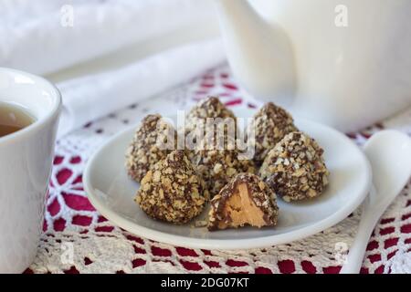 Hausgemachtes köstliches Dessert. Bonbons aus Erdnussbutter mit Schokoladenglasur und Wafer-Krume mit Tee auf einer Spitzentischdecke, selektiver Fokus Stockfoto