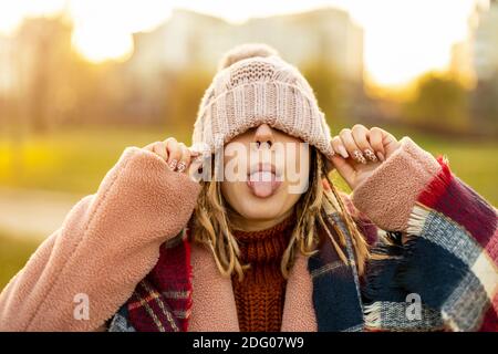 Verspielte Frau, die die Augen mit Strickmütze bedeckt, die aus der Zunge ragt Stockfoto