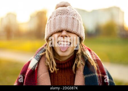 Verspielte Frau, die die Augen mit Strickmütze bedeckt, die aus der Zunge ragt Stockfoto