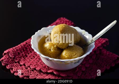 Die berühmtesten bengalischen oder indischen Süßigkeiten - Rasgulla gemacht Mit Dattelpalmenjaggery oder nolen gur in einer Schüssel Auf dunklem Hintergrund Stockfoto