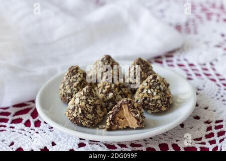 Hausgemachtes köstliches Dessert. Bonbons aus Erdnussbutter mit Schokoladenglasur und Wafer-Krume auf einer Spitzentischdecke, selektiver Fokus Stockfoto