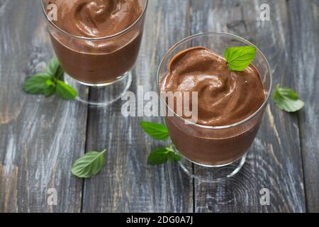 Zwei Gläser mit köstlicher veganer Schokoladenmousse aus Banane mit Kakao und Minze auf einem Holztisch, selektiver Fokus Stockfoto