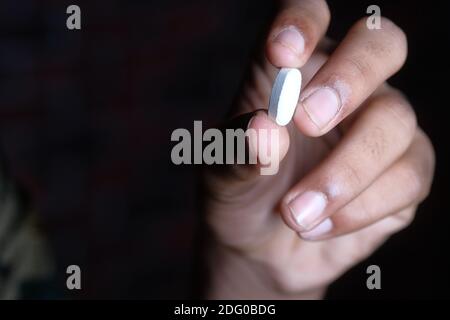 Nahaufnahme der Hand eines Mannes, der eine Pille auf Schwarz hält Hintergrund Stockfoto