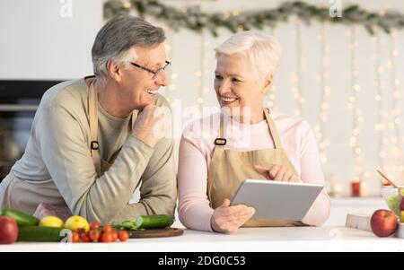 Seniorenpaar Mit Tablet-Computer Vorbereitung Weihnachtsessen In Der Küche Stockfoto