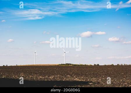 Windturbinen am Horizont hinter dem Feld gegen den blauen Himmel. Industrielle Landschaften der Ukraine. Stockfoto