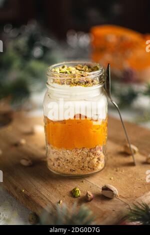 Kürbisparfait mit Pistazien in Glas Mason Jar Becher auf einem Holzbrett, einen Löffel, vor einem Hintergrund der Neujahrsdekoration Stockfoto