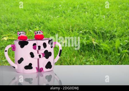 Natur des Milchprodukts. Lustige Kühe umarmen sich gegenseitig als Form von zwei Tassen auf dem Tisch über natürlichen Hintergrund. Werbevorlage für Ihre Lebensmittel und Produkte Stockfoto