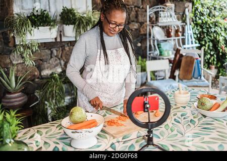 Afrikanische ältere Frau Kochen im Freien, während Online-Streaming für Webinar Masterclass Unterricht zu Hause - Food und Influencer Konzept - Fokus auf Gesicht Stockfoto