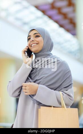 Vertikale Taille nach oben Porträt von lächelnden Nahost-Frau sprechen durch Smartphone beim Einkaufen im Einkaufszentrum Stockfoto