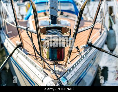 Nahaufnahme des Bugs eines Segelbootes, das in einem Yachthafen verankert ist, mit Leinen, Seilen und Navigations-Laterne im Fokus. Stockfoto