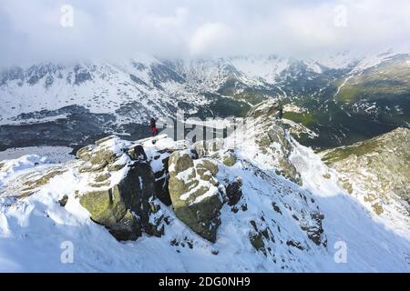 Landschaft am kalten Wintermorgen. Fröhlicher Tourist in Sportkleidung steht am Rande des Abgrunds. Hohe Berge mit schneeweißen Gipfeln. S Stockfoto