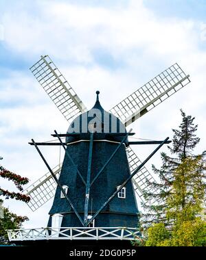 Alte Windmühle aus schwarzem Holz, die früher zum Mahlen von Mehl verwendet wurde. Mit Wolken und blauem Himmel im Hintergrund. Stockfoto