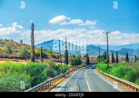 Landschaft von Zypern mit Autos Fahrzeuge Reiten Asphaltstraße im Tal mit gelben trockenen Feldern, Zypressen und Straßenpfosten, Troodos Gebirge Stockfoto