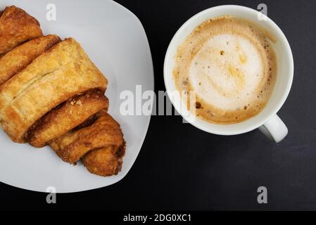 Direkt über dem Blick auf Franzbrotchen Gebäck und Tasse Kaffee auf dunklem Tisch, Franzbroetchen sind ein süßes Zimtgebäck und eine lokale Delikatesse in und Stockfoto