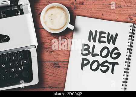 Text NEW BLOG POST geschrieben auf Spiralnotizblock auf Tisch mit Schreibmaschine und Tasse Kaffee, Blogging und Journalismus Konzept Stockfoto