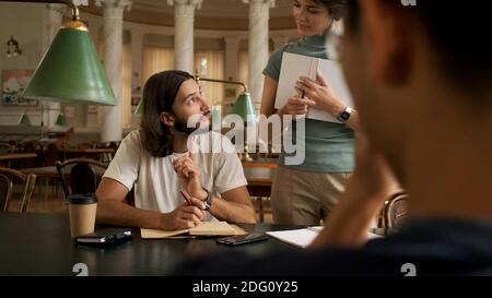 Junger Student, der mit Tutor in der Bibliothek studiert. Studenten sitzen zusammen Bücher lesen. Junge Leute, die sich auf Prüfungen in der Universitätsbibliothek vorbereiten Stockfoto