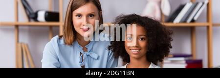Glücklich multikulturelle Psychologin und Mädchen Blick auf Kamera auf verschwommenem Hintergrund, Banner Stockfoto