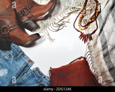 Boho-Stil. Lederstiefel, Holzkette, Denim Shorts und Hippie Tasche mit Fransen auf weißem Hintergrund. Overhead-Ansicht der Casual Day Outfits für Frauen. Stockfoto