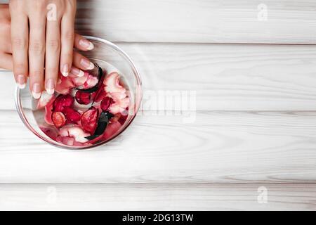 Sanfte Natürliche Maniküre, Handpflege. Einweichen Fingernägel im Bad mit Kräuteröl und Blumen auf weißem Holztisch mit Copy Space Stockfoto