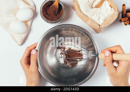 Draufsicht auf weibliche Hände Mehl und Kakaopulver in Schüssel schlagen, um hausgemachten Schokoladenkuchen zu kochen. Stockfoto