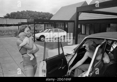 Großbritannien der 1970er Jahre, professionelles Ehepaar mit mittlerem Einkommen außerhalb ihres neuen modernen Hauses auf einem kürzlich erbauten neuen Wohngebiet, einer modernen Entwicklung. Mit dem neuen Baby in den Armen an seinem Auto hängen, das vor ihrem Haus 1977 England geparkt ist. Milton Keynes Buckinghamshire HOMER SYKES Stockfoto