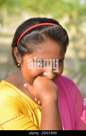 Nahaufnahme eines indischen Dorf Teenager-Mädchen lächelnd mit Blume in der Hand und trägt Haarband und Gold Ohrring Stockfoto