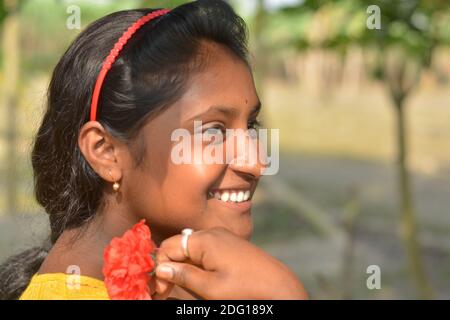 Nahaufnahme eines indischen Dorf Teenager-Mädchen lächelnd mit Blume in der Hand und trägt Haarband und Gold Ohrring Stockfoto