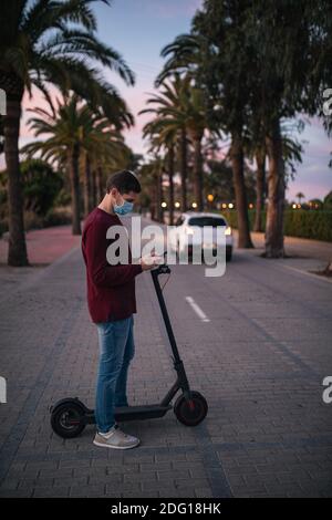 Junger Mann steht mit seinem E-Scooter auf der Straße, um die Straße zu überqueren. Konzepttechnologie. Stockfoto