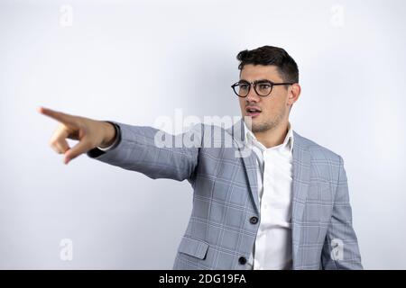 Business junger Mann trägt Anzug über weißem Hintergrund zeigt mit Finger überrascht voraus, offenen Mund erstaunt Ausdruck, etwas auf der Vorderseite Stockfoto