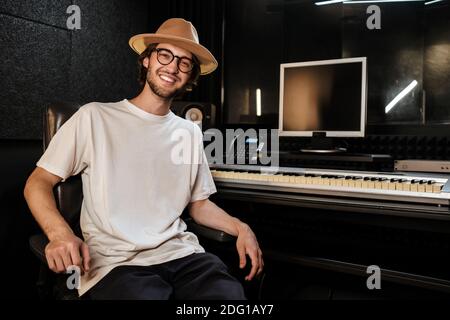 Gutaussehender fröhlicher Kerl glücklich in der Kamera in modernen Tonaufnahme Studio suchen. Junger Musiker, der im Studio arbeitet Stockfoto